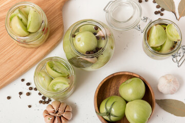 Green tomatoes for canning in a glass jar on a light wooden background. Unripe tomatoes for harvest.