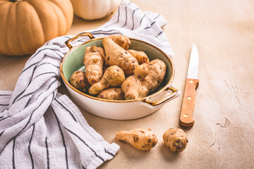 Raw topinambour with pumpkins in bowl on kitchen table