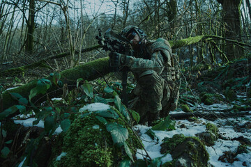 Portrait of airsoft player in professional equipment in helmet aiming at victim with gun in the forest. Soldier with weapons at war