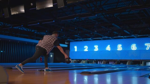 Caucasian Man in bowling throws a ball in slow motion and knocks down skittles. Play bowling. Throw balls on the floor of the bowling club