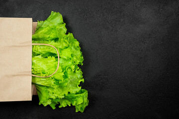 Fresh lettuce leaves in a paper bag on a black background. - obrazy, fototapety, plakaty