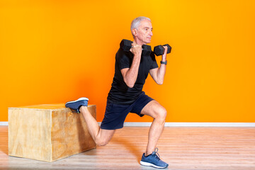 focused senior fit man doing weight lifting workout exercise staning at the gym isolated on orange background. mature people fitness training indoor. elderly person recovery healthy lifestyle concept