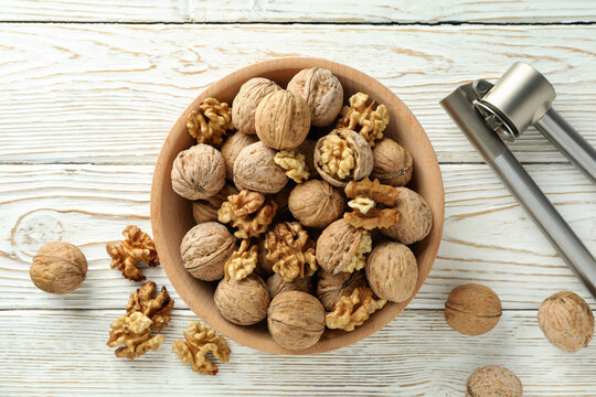 Nutcracker and bowl of walnuts on white wooden background