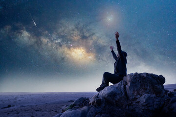 unknown person sitting on the rock with open arms or hands up under the Milky Way at night...