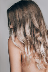 Close-up of the wavy blonde hair of a young blonde woman isolated on a gray background. Result of coloring, highlighting, perming. Beauty and fashion. Vertical shot