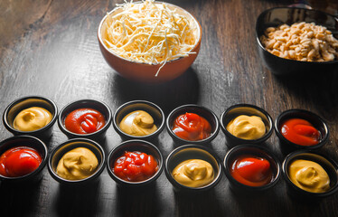 Small cups with ketchup and mustard, a cup with cheese shavings stand in a row on the table.