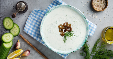 Traditional Greek sauce Tzatziki. Yoghurt, cucumber, dill, garlic and salt oil in a ceramic bowl on a gray stone or concrete background. Rustic style. Selective focus. Top view