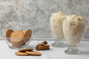 two glasses of rice pudding with cookies and cinnamon on a table with white tablecloth
