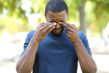 Man with black skin scratching itchy eyes in a park