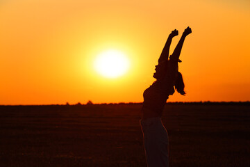 Fototapeta na wymiar Profile of excited woman raising arms at sunset