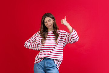 Emotional young beautiful girl in sweater and jeans posing isolated on red studio background. Concept of emotions, facial expression