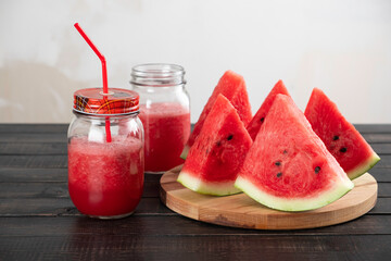 red smoothie made of pulp in glass jars with a lid and a drinking tube with triangular slices of watermelon on a wooden table