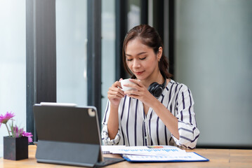 Beautiful young Asian businesswoman drinking a coffee working on laptop at office.