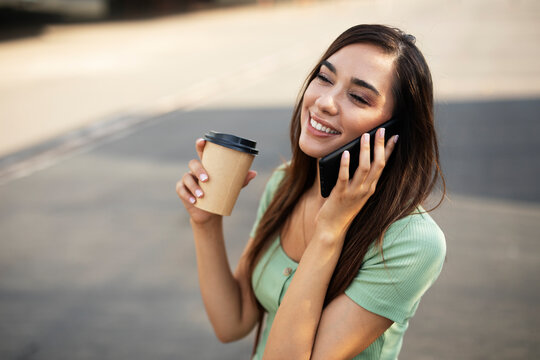 Young girl with coffee to go holding smartphone. Beautiful woman talking to the phone while enjoying in fresh coffee.