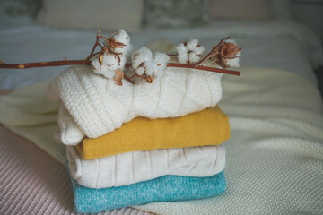 Fototapeta na wymiar Stack of knitted warm sweaters in wicker rattan basket, plaid, branch of cotton. Autumn mood.