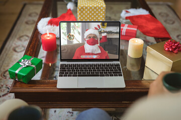 Senior caucasian man in santa costume and face mask on laptop video call screen at christmas