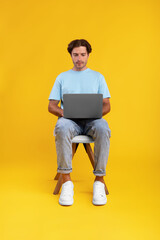 Serious guy using laptop sitting on chair at studio