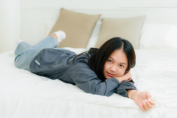 Portrait Asian cute long-haired teen wearing a gray long sleeve shirt Lay back and relax in bed in the bedroom happily.