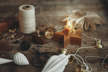 Christmas candle, bells, ornaments, pine cones, thread and scissors on rustic wood. Moody image