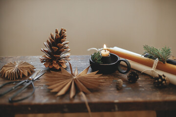 Merry Christmas! Christmas candle, paper stars, pine cones, scissors on rustic wood. Scandi hygge