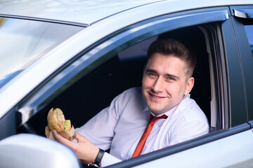 A man in a suit drinks coffee and eats a burger in the car.