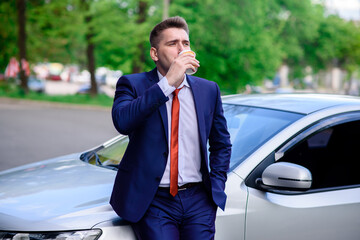 A businessman drinks coffee near his car