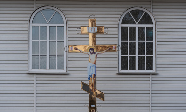 Gilded Christian cross with the image of the crucified Jesus Christ against the background of the church facade. Church windows