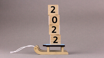 Wooden cubes with numbers 2022 on toy wooden sleds on gray background