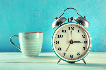 Good morning greeting card in teal tones. A vintage alarm clock and a cup of coffee on a blue background with a place for text