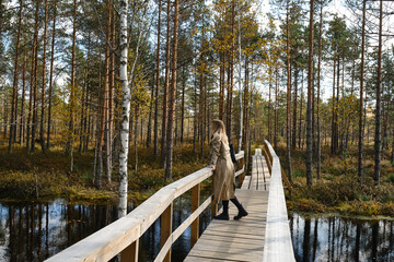 A girl in trench coats stands on a bridge in the park and enjoys the view. Reunion with nature on...