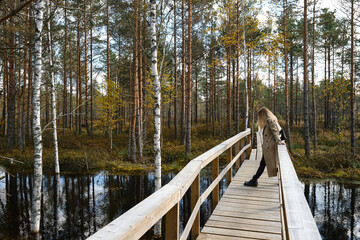 A girl in trench coats stands on a bridge in the park and enjoys the view. Reunion with nature on...