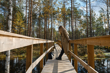 A girl in trench coats stands on a bridge in the park and enjoys the view. Reunion with nature on...