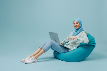 Full size young arabian asian muslim woman in abaya hijab sit in bag chair hold use work point on...