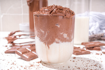 Whipped dalgona coffee styled hot chocolate, modern cocoa creamy drink, with chocolate slices on kitchen home table copy space