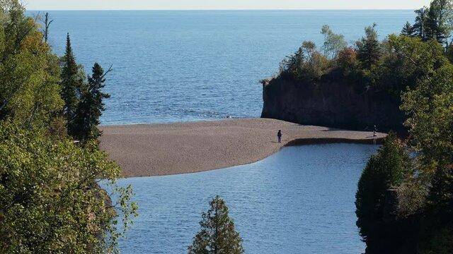Mouth of the Baptism River where it enters Lake Superior in Minnesota, with a couple people fishing from as sandbar. At Tettegouche State Park on the shore of one of the Great Lakes.