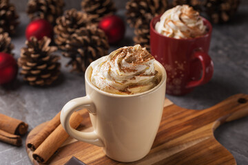 Pair of mugs filled with hot chocolate or a coffee and whipped cream on a dark stone table. Christmas and New Year's composition. Holiday Decorations. Close up with shallow dof.