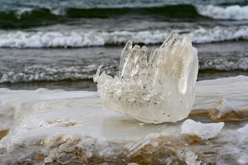 A piece of ice resembling a fist on the shore of a lake with waves