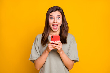 Portrait of pretty amazed cheerful brown-haired girl using device notification isolated over bright yellow color background