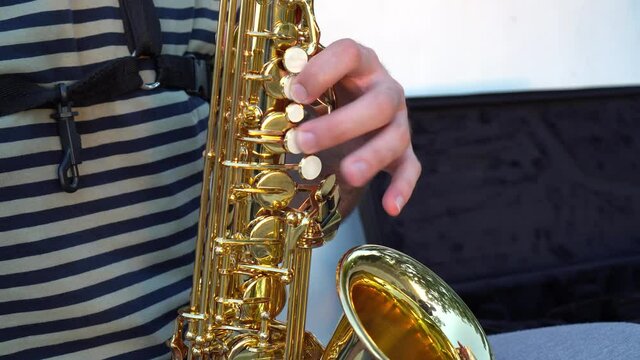 Close up of the hands of a musician playing alto saxophone next to the musical instrument case. Details of saxophonist playing sax.