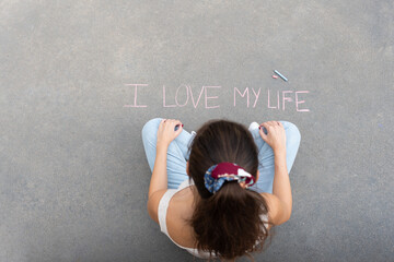 Young girl with pigtail and dressed in blue jeans sitting on the floor, paints a brooding reflexion...