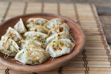 Gyoza with sesame seeds and micro greens in a ceramic bowl with bamboo sticks on a wooden table. Rustic style. Traditional Orietnal food concept. Copy space. Selective focus.