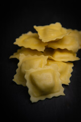 Tasty raw ravioli with flour and spinach on dark background, process of making italian ravioli