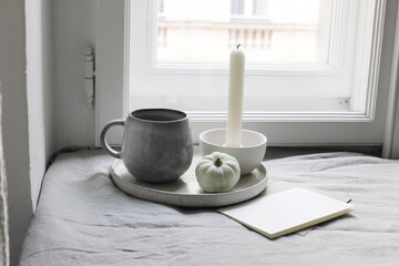 Autumn still life. White little pumpkin, cup of coffee and blank greeting card mockup near window. Candle with white ceramic candleholder. Moody fall interior composition. Halloween, Thanksgiving.