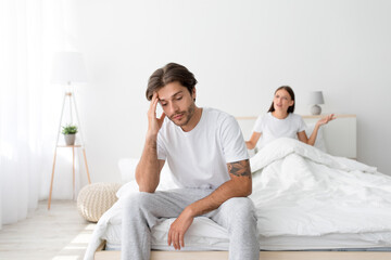 Angry resentful upset millennial caucasian wife sits on bed, quarreling husband, shouting and dispute