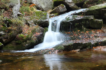 Fototapeta na wymiar Waterfall in the mountains in the woods on a small mountain stream between the rocks in autumn
