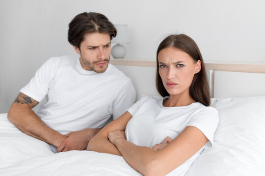 Unhappy millennial european guy calm offended woman with crossed hands on chest on bed in bedroom interior