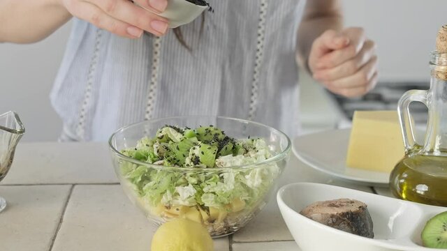 Woman adding sesame seeds in salad. Process of preparing salad from tuna, cabbage, cheese and kiwi. Healthy food. Close-up in 4K, UHD