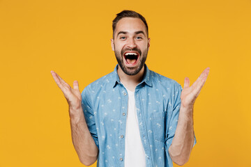 Young happy joyful fun surprised overjoyed excited caucasian man 20s wear blue shirt white t-shirt spread hands scream isolated on plain yellow background studio portrait. People lifestyle concept - obrazy, fototapety, plakaty