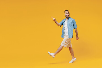 Fototapeta na wymiar Full body young smiling happy cheerful satisfied man 20s wear blue shirt white t-shirt walking going stroll point index finger aside on workspace isolated on plain yellow background studio portrait