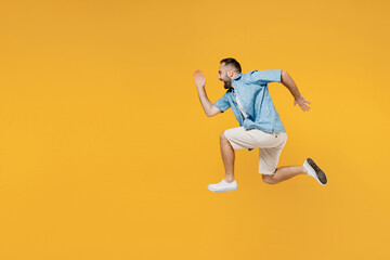 Fototapeta na wymiar Full body side view young smiling sporty happy caucasian man 20s in blue shirt white t-shirt run fast jump high hurry up isolated on plain yellow background studio portrait. People lifestyle concept.